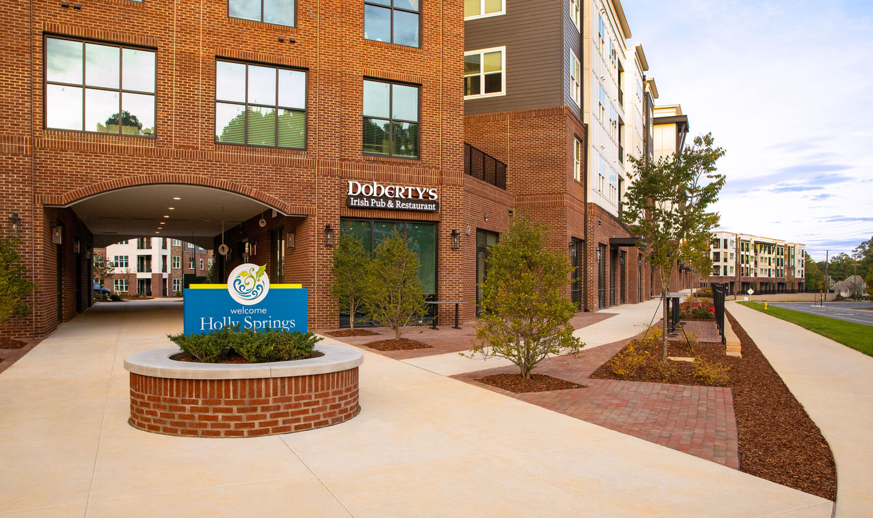 Peterson Station at Sunset Lake mixed-use building featuring brick veneer, paver walkways, and the Holly Springs welcome sign.