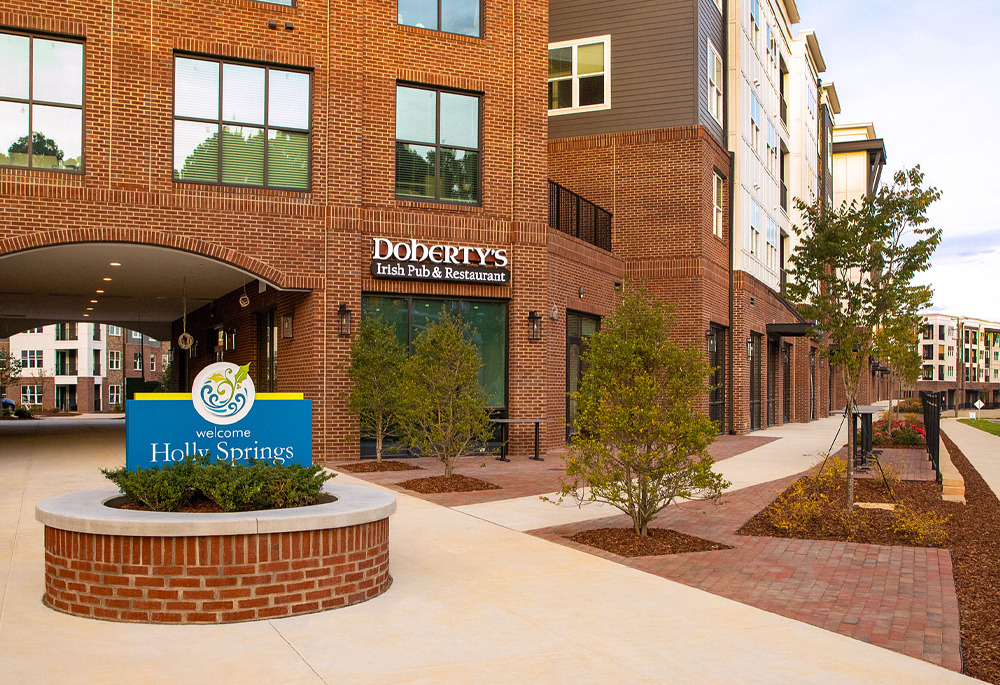 Peterson Station at Sunset Lake mixed-use building featuring brick veneer, paver walkways, and the Holly Springs welcome sign.